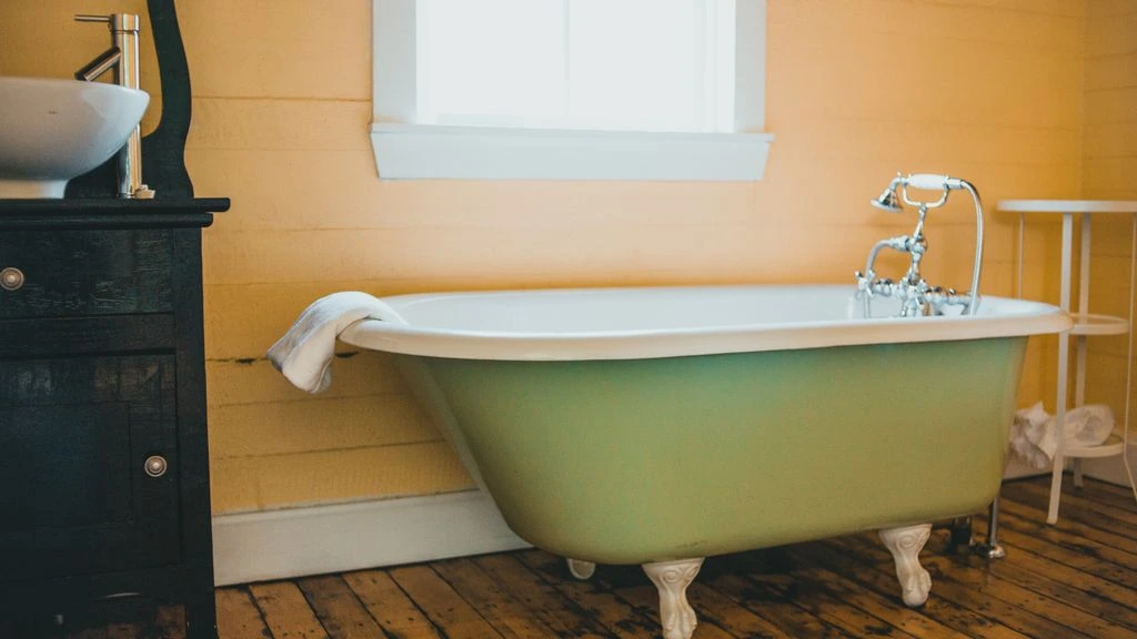 A bath ready to begin — apothecary bottle and scattered botanicals by a bathtub